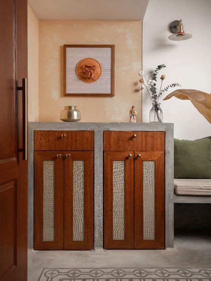 The foyer features a custom-designed shoe cabinet with rattan-paneled doors, set within a concrete-finished base. This unit provides practical storage at the entrance.