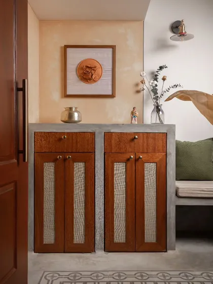 The foyer features a custom-designed shoe cabinet with rattan-paneled doors, set within a concrete-finished base. This unit provides practical storage at the entrance.
