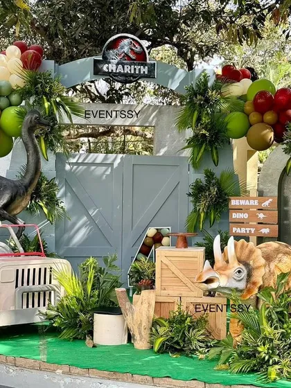 A full Jurassic Park setup, complete with realistic dinosaur props, a themed jeep, and jungle foliage, all set around a water feature.