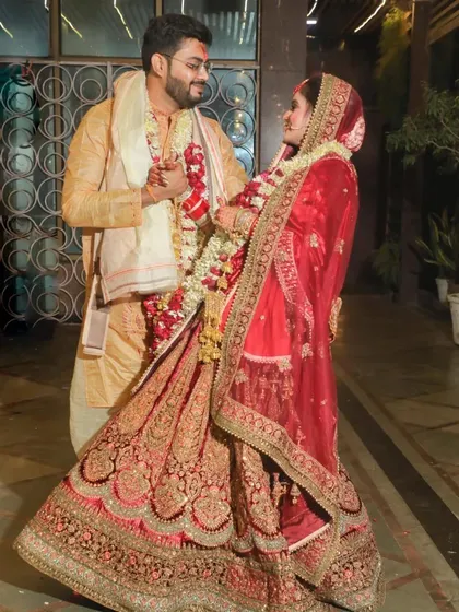 A classic wedding day pose with a candid feel. The couple faces each other, sharing a private moment amidst the celebrations. This shot beautifully captures the bride's flowing red lehenga and the groom's coordinated outfit, highlighting their connection.