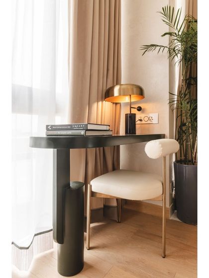 A small, elegant desk and chair create a functional workspace by the window. The design is consistent with the apartment's modern Art Deco theme, featuring sculptural forms and a mix of materials.