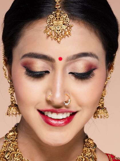 A joyful close-up of a bride, capturing her smile and the beautiful details of her traditional nose ring and maang tikka.