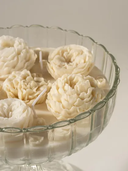 A close-up of an intricate, flower-shaped candle from Doro. The focus on the delicate wax petals highlights the artistry and craftsmanship of the product.