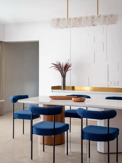 We love adding a pop of color to create drama and personality. In our 'Vishu Home' project, these bold, royal blue velvet chairs stand out against the monolithic white dining table and textured wall, creating a modern yet timeless dining experience that is both elegant and inviting.