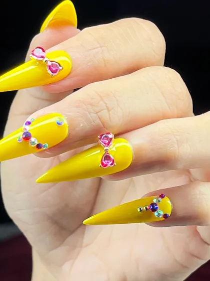 A bright and cheerful yet elegant design, with vibrant yellow stiletto nails adorned with carefully placed pink and purple rhinestones.