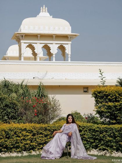 A portrait of the bride seated in a garden, her lavender gown contrasting beautifully with the green foliage and white architecture of the palace.