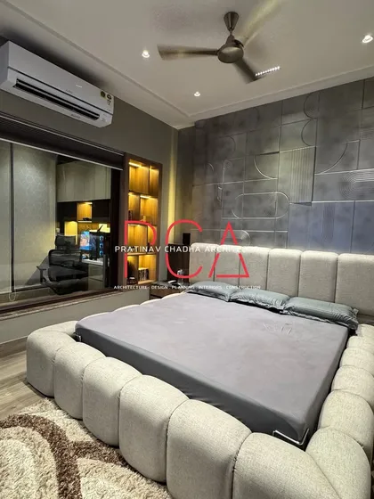 A wider view of the son's bedroom, showing the relationship between the bed, the accent wall, and the large window. The design balances bold features with soft, comfortable textiles.