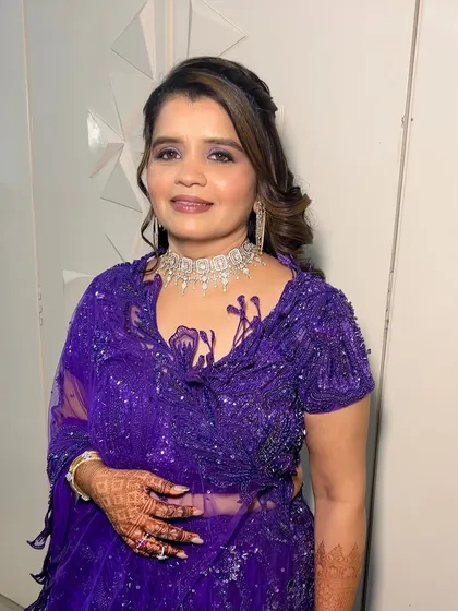 A full-length view of a stunning guest makeup look. The purple sequined saree is complemented by a shimmery purple smokey eye, creating a cohesive and glamorous style.