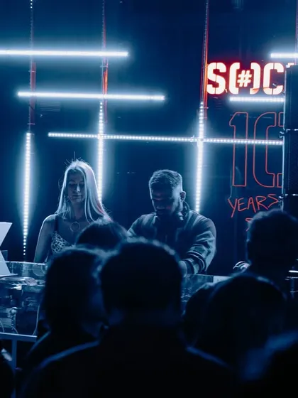 A blue-lit shot from the same event, showing me and a fellow artist on the decks.