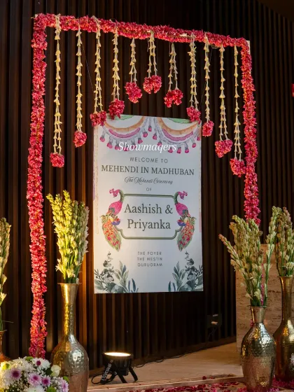 The personalized welcome sign for the 'Mehendi in Madhuban' ceremony, framed by hanging floral strings.