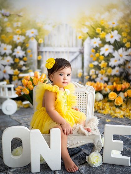A beautiful first birthday portrait in a sunny yellow garden, complete with daisies and tulips.