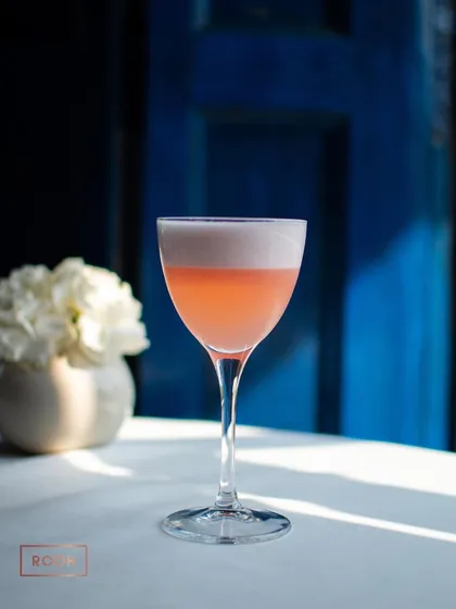 Sipping on summer. This elegant, pastel-colored sour cocktail is a sophisticated choice for a warm evening, served in a classic coupe glass.