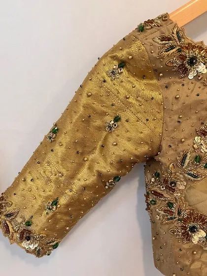A close-up of the sleeve of the gold bridal blouse, showing the detailed beadwork and sequins that add a touch of color and sparkle.