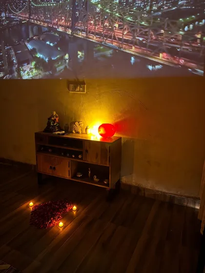The living room is set up for a cozy movie night, with candles and rose petals on the floor adding to the romantic ambiance.