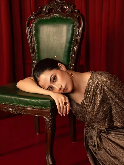 A moody and emotive shot from a party wear campaign. The model's pose, leaning against a vintage chair, creates a sense of introspection and drama.