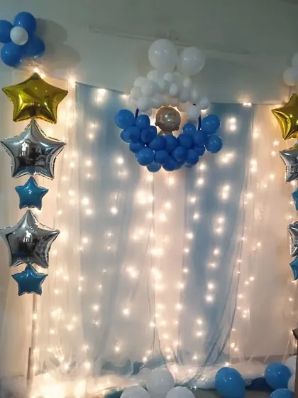 A dreamy backdrop created with a sheer white curtain and fairy lights. The decoration is enhanced with blue and white balloon arrangements and star-shaped foil balloons.