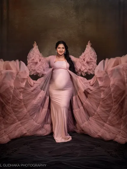 A powerful and symmetrical pose showcasing the full, dramatic spread of the pink ruffled gown. This shot emphasizes the grandeur of the dress and the confident presence of the mother-to-be.