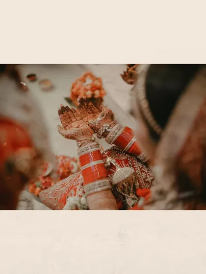A close-up of the bride's hands during a ritual, her intricate henna and red choora symbolizing her new marital status.