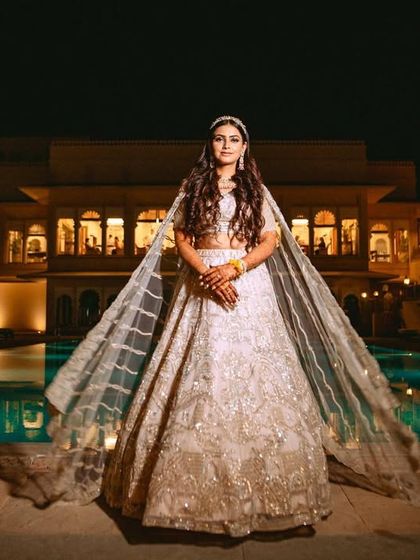 A stunning wide shot of the bride by the pool at night, her flowing lehenga creating a dramatic and royal silhouette.