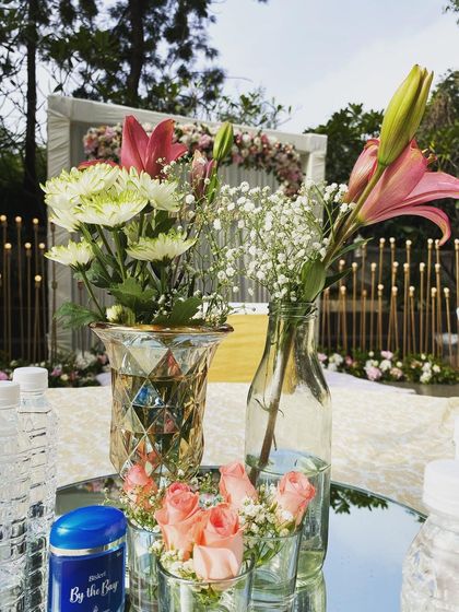 A simple yet beautiful detail. Small vases of fresh flowers, including lilies and roses, add a touch of elegance to a guest table at an outdoor event.
