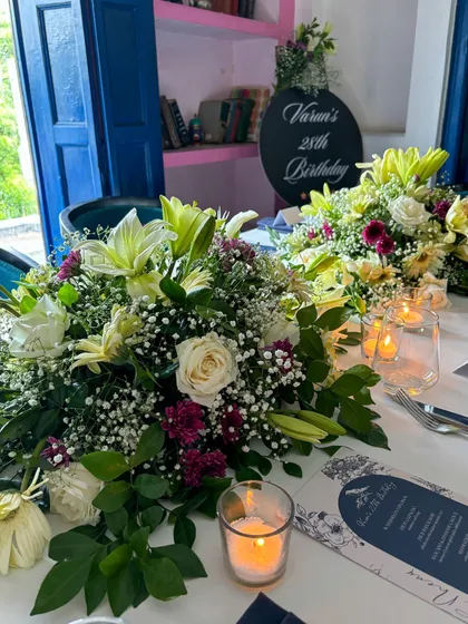 The table is set for a memorable birthday feast. The combination of lilies, roses, and soft candlelight creates a warm and inviting atmosphere for guests.