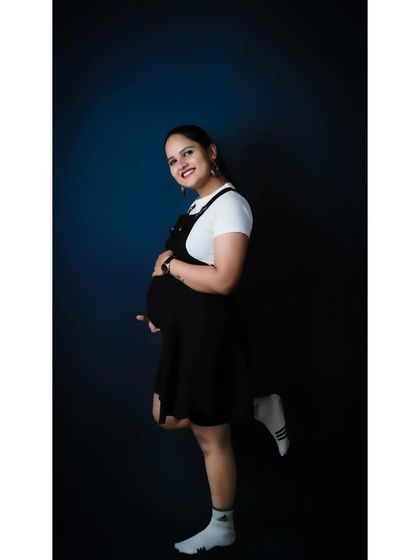 A full-length version of a playful solo studio portrait. The casual outfit and happy pose create a modern and fun image that showcases the mom-to-be's personality.
