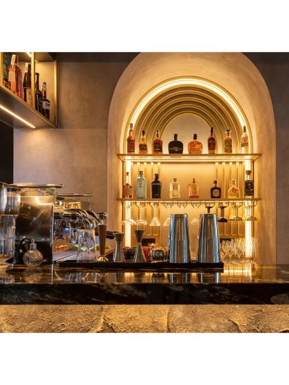 A close-up of the bar area, showing the elegant back-lit shelving within a golden arch. The design combines functionality with a touch of glamour, perfect for showcasing premium spirits.