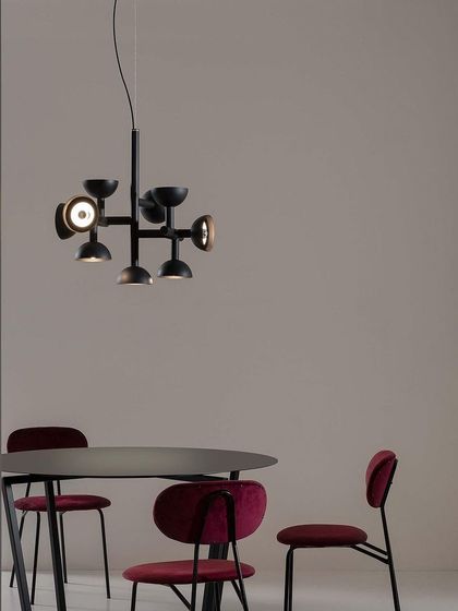 The black Sibilla chandelier provides a strong, graphic focal point in a dining area with deep red chairs.