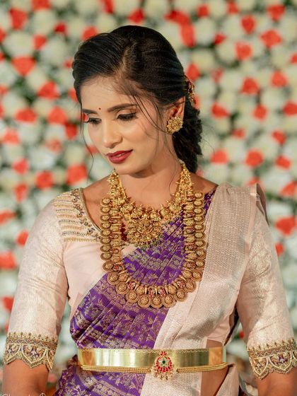 A bride in a purple and white saree with a simple yet elegant embroidered blouse. The look is completed with traditional gold jewelry.