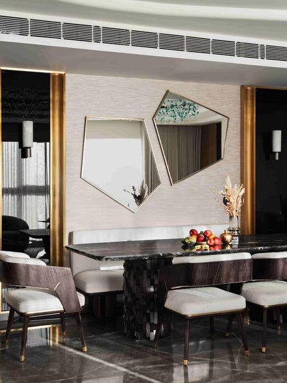 The dining area in the 'RYSA' residence in Mumbai is a study in contemporary elegance, with a sculptural table base, custom seating, and geometric mirrors.