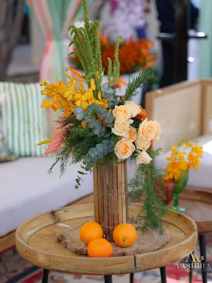 A centerpiece detail, with a bamboo-style vase holding peach roses and tropical greenery, complemented by fresh oranges on a wooden tray.