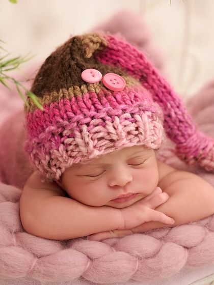 A detailed close-up of a newborn's peaceful face, wearing an adorable pink and brown hand-knitted hat, nestled in a cozy pink basket.