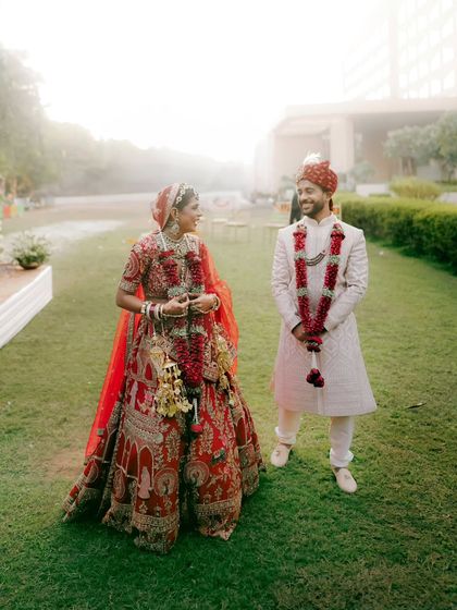 A candid moment of the couple sharing a smile in the garden after their ceremony, their traditional attire vibrant against the green lawn.