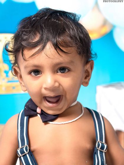 A little prince celebrating his first birthday with a royal blue cake smash. The setup includes a crown, balloons, and a delicious-looking cake ready to be smashed.