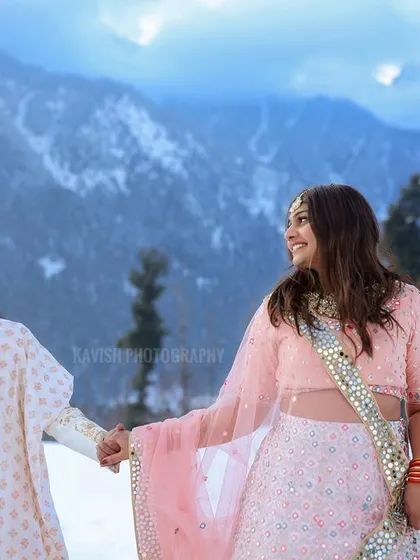 A candid moment of the couple holding hands and smiling, walking through the snow. Their traditional attire contrasts beautifully with the winter landscape in this pre-wedding picture.