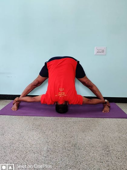 Prasarita Padottanasana with hands gripping the ankles to pull the torso deeper into the stretch.