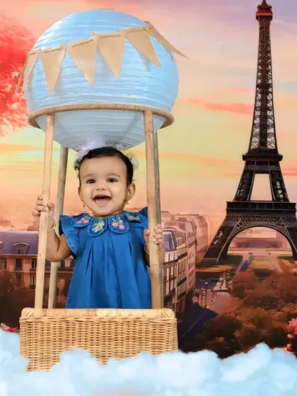 A happy baby girl enjoys a ride in a hot air balloon over Paris, with the Eiffel Tower glowing in the background.