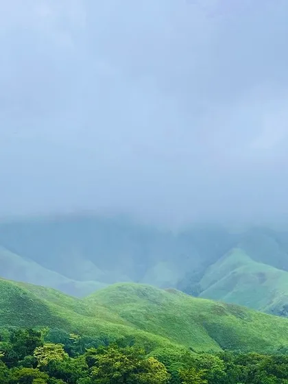 The rolling green hills of the Western Ghats under a cloudy sky.