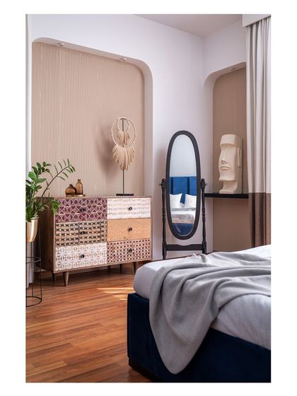 Inspired by the clients' love for art, this bedroom features niches displaying sculptures reminiscent of Moai statues. The design pairs a deep blue bed with a patterned chest of drawers, creating a space with a unique and artistic character.