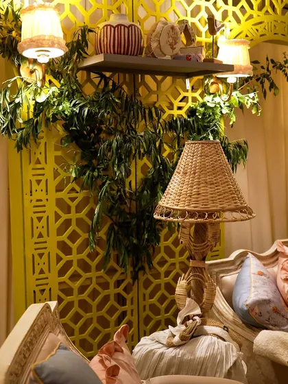 A close-up of a wicker lamp and other decor details against a yellow jaali screen.