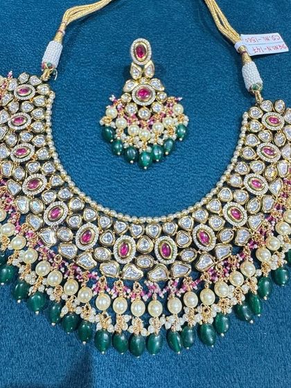 A beautiful bib-style necklace featuring fine kundan work, pearls, and a mix of ruby and emerald colored stones.