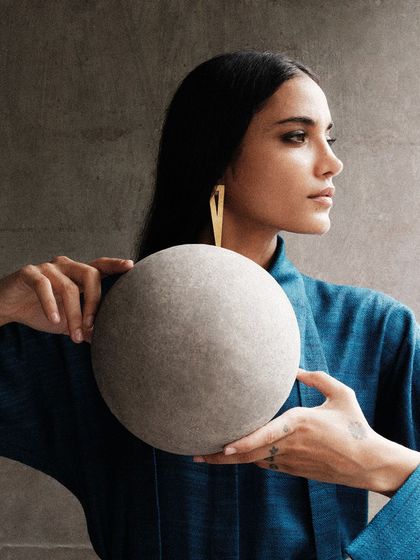A portrait where the model holds a stone sphere, connecting her to the materials of the architectural environment. This adds a conceptual layer to the campaign.