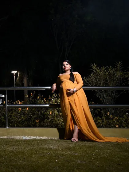 A dramatic and elegant pose from an evening outdoor maternity session. The flowing yellow gown looks stunning against the dark, natural background.