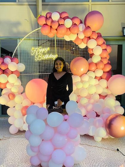 A full-length shot of the birthday girl enjoying her elegant party setup with a flowing arch of pink and white balloons.