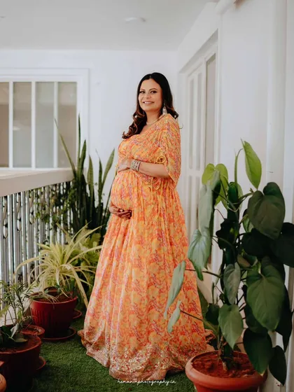 A full-length portrait of the mother-to-be on her home balcony, surrounded by lush plants. This shows how we can use your own space to create beautiful and personal maternity photos.