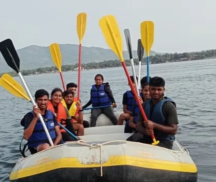A group in a small inflatable boat raises their paddles, full of energy and excitement during a session at Karwar.