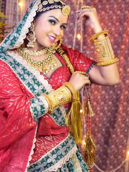 A smiling model in a vibrant Rajasthani bandhani outfit, adorned with traditional gold-look jewellery including heavy bangles and a borla.