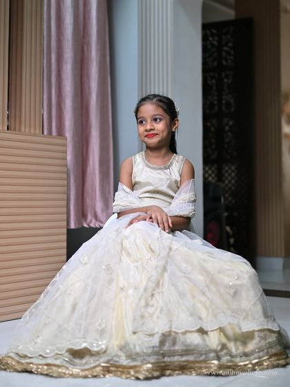 A seated pose of a young girl in the full ivory lehenga, showing the beautiful flare of the skirt and the delicate sequin work.