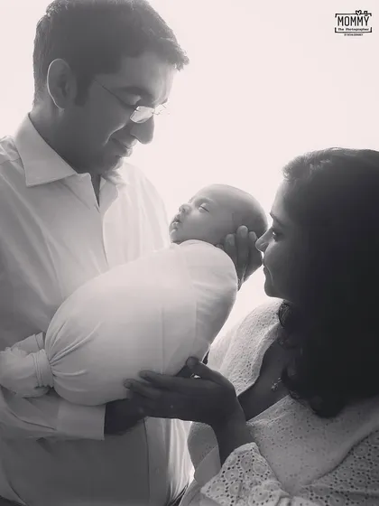 A gentle and loving portrait of new parents admiring their baby. The soft, high key lighting in this black and white image creates a dreamy and emotional mood.