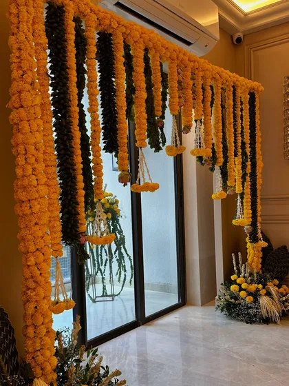 A full view of the marigold and mango leaf toran framing a doorway. This is a classic decoration for auspicious occasions, symbolizing prosperity and good fortune.